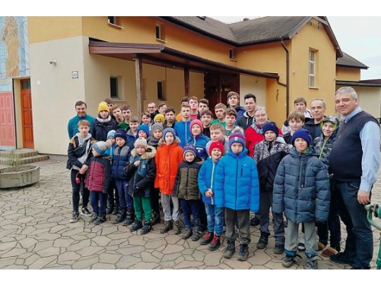 Kindergruppe mit Pater und anderen Erwachsenen vor einem Gebäude 