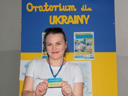 junge Frau zeigt lächelnd Schild in den Farben der ukrainischen Flagge 