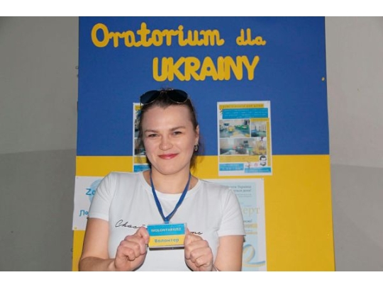 junge Frau zeigt lächelnd Schild in den Farben der ukrainischen Flagge 