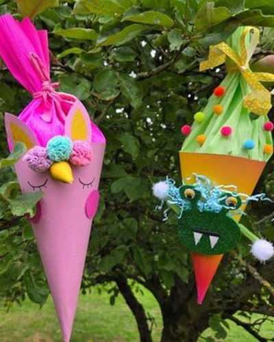 Kleine Schultüten in pink und und orange mit Augen, Zähnen und Pompons hängen in einem Baum