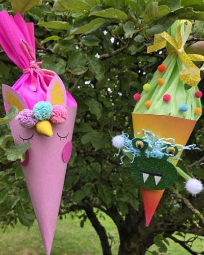 Kleine Schultüten in pink und und orange mit Augen, Zähnen und Pompons hängen in einem Baum