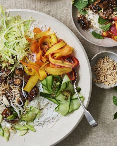 Salat mit Karotten, Gurken, Fleisch und Reisnudeln auf Teller, daneben Schälchen mit Thai-Basilikum und Erdnüssen