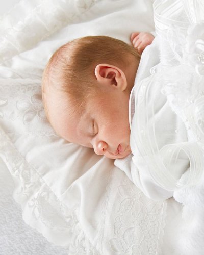 Schlafendes Baby im weißen Kleid liegt auf weißem Kissen