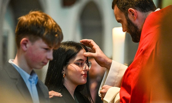Priester zeichnet einer Jugendlichen mit Chrisamöl ein Kreuz auf die Stirn