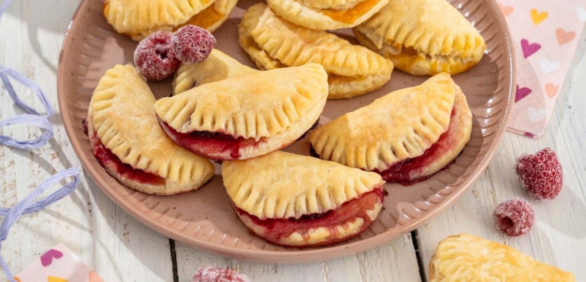 Quarktaschen mit roter Füllung und einzelne Himbeeren auf Schale