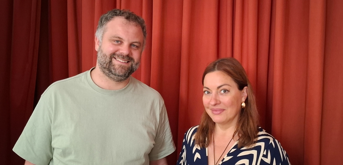 Christian Huber und Julia Dahmen lächeln vor einem roten Vorhang in die Kamera.