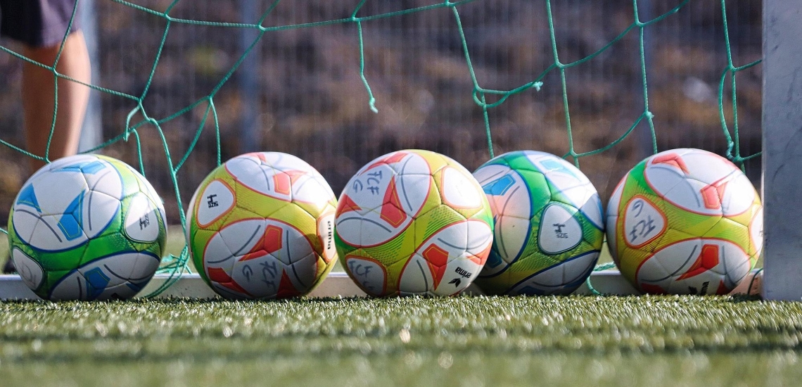 Fünf Fußbälle liegen in einer Reihe in einem Tor