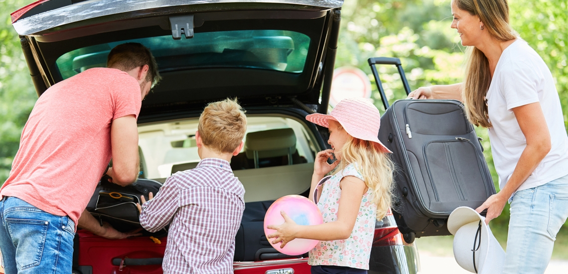 Eltern und Kinder packen Gepäck in den Kofferraum.