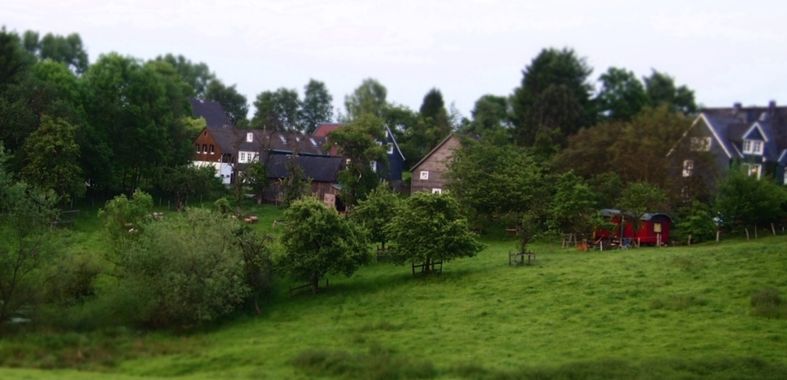 Häuser im bergischen Stil und ein roter Schäferwagen inmitten von grünen Hügeln