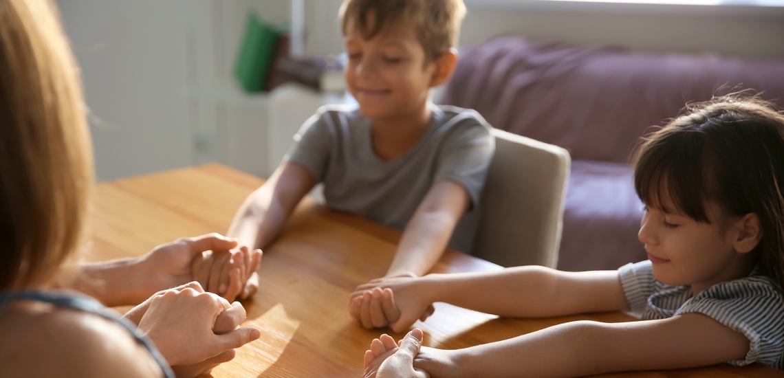 Zwei Kinder beten mit Eltern - alle halten sich an den Händen