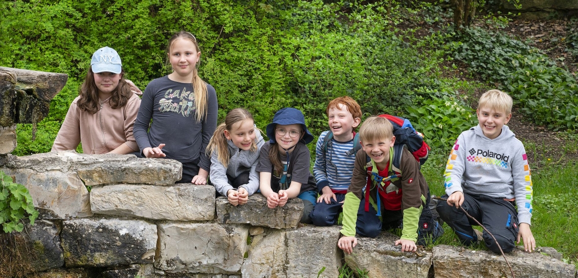 Kinder lehnen lachend in einer Reihe über einer Natursteinmauer auf dem Gelände des Klosters Ensdorf