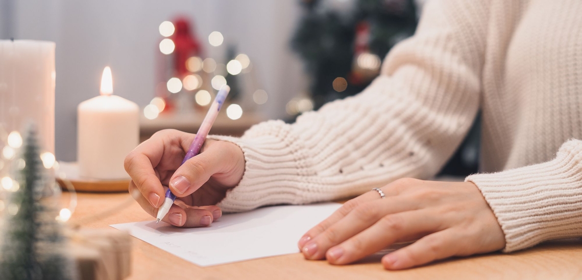 Hände von Frau mit Stift und weißem Blatt Papier, im Hintergrund Weihnachtskerzen und Lichter