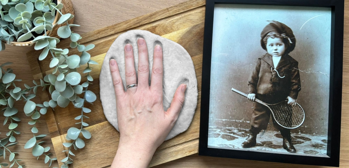 Hand drückt sich flach in Modelliermasse, daneben altes, schwarzweißes Foto eines Kindes