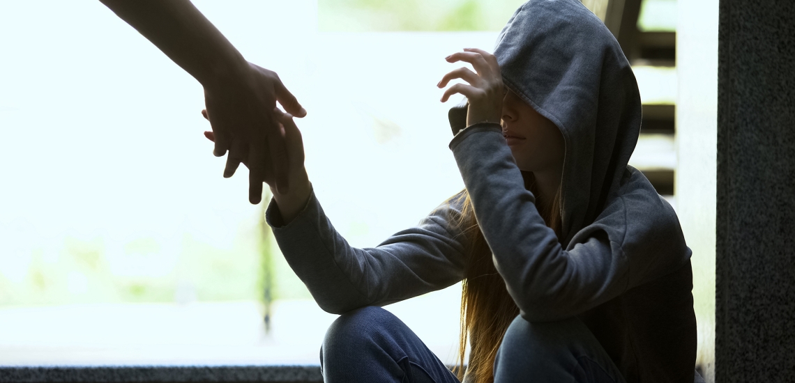 Junge Obdachlose mit Kapuze ergreift eine Hand, die ihr hingestreckt wird.