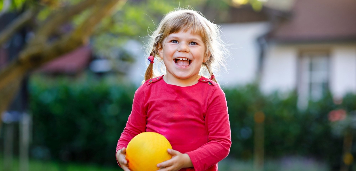 Kleines Mädchen mit Zöpfen lachend draußen mit Ball