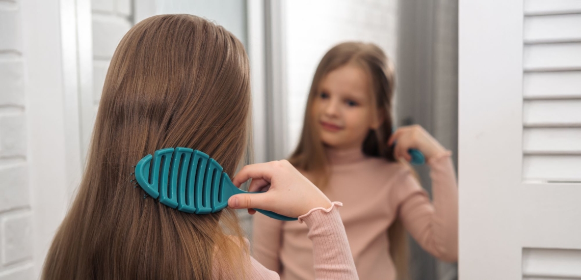 Mädchen bürstet sich vor dem Spiegel die langen dunkelblonden Haare