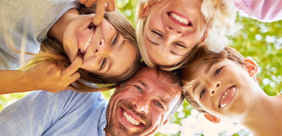 Tochter und Sohn schneiden Grimassen, die Eltern lachen mit ihnen darüber.