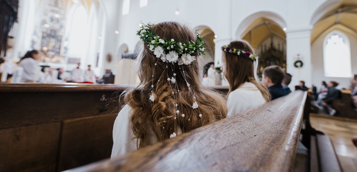 Erstkommunionkinder in festlicher Kleidung sitzen während des Gottesdienstes in einer Kirchenbank