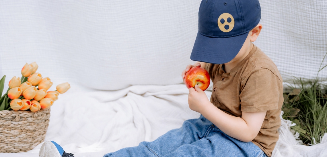 Ein Kind mit einer Baseballkappe mit Blindenzeichen betastet einen Apfel