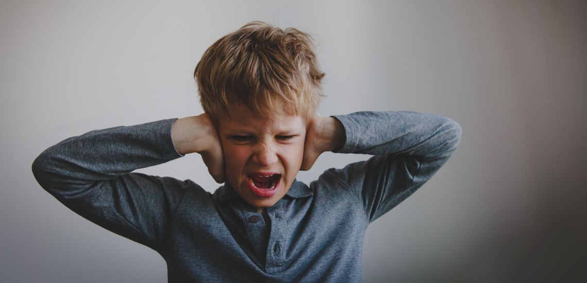 Junge hält sich die Ohren zu und schreit wütend
