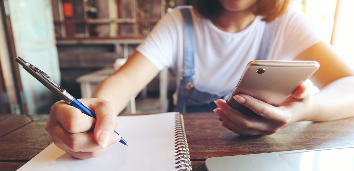 Jugendliche am Tisch mit Smartphone, Laptop, Notizblock und Stift