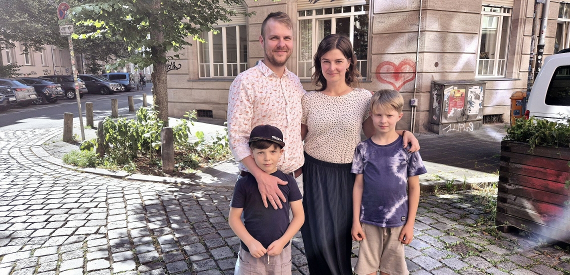 Vater, Mutter und zwei Kinder auf der Straße vor einem Haus in einer Großstadt