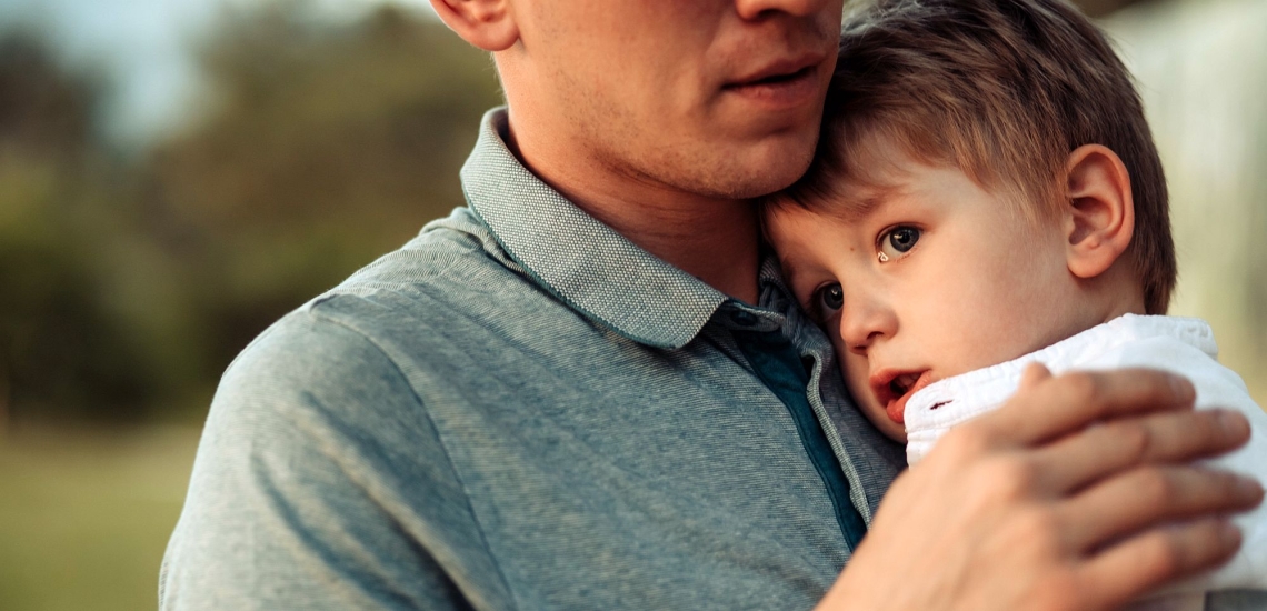 Vater hält Kind, das Tränen in den Augen hat, liebevoll im Arm