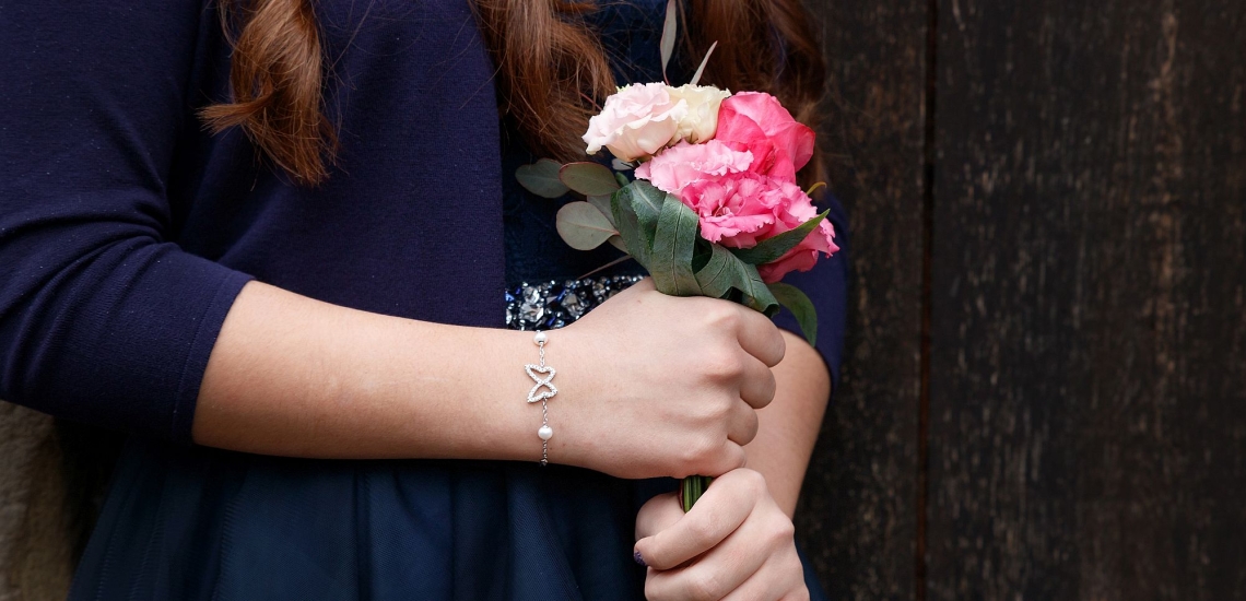 Jugendliche in dunkelblauem Kleid mit Armkettchen und kleinem Blumenstrauß in der Hand