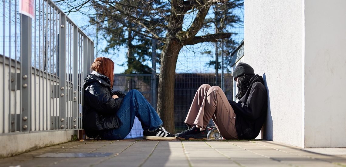 Zwei obdachlose Mädchen sitzen auf dem Boden einander gegenüber.