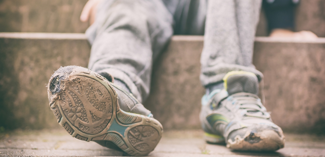 Füße eines Kindes mit grauer Jogginghose und kaputten Schuhen