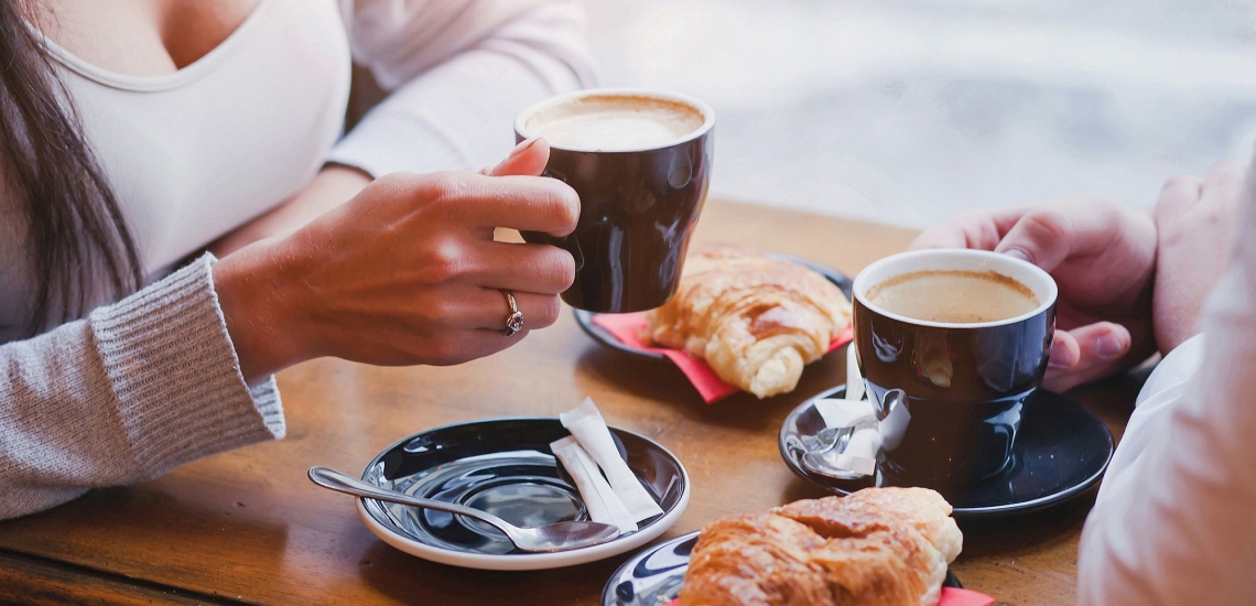 Tisch mit Kaffeetassen und Croissants, Hände und Oberkörper von zwei Frauen, die am Tisch sitzen