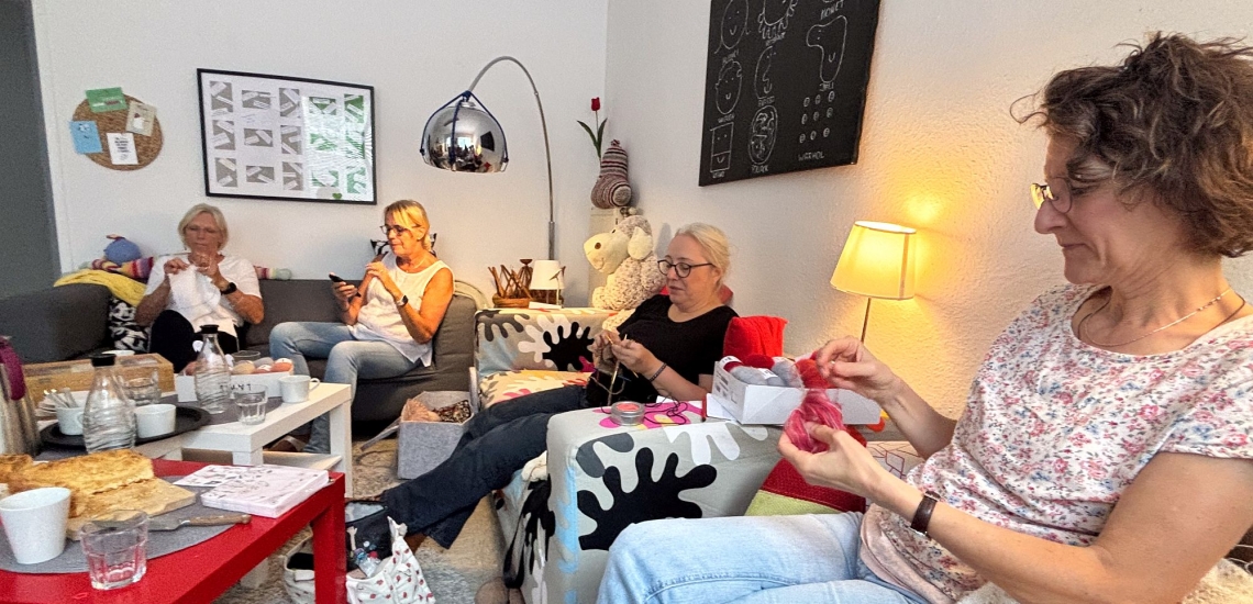 Frauen sitzen gemütlich auf Sofas und Sesseln und stricken