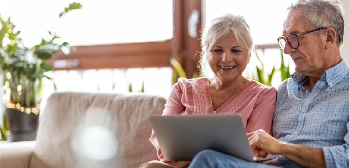 Älteres Paar sitzt entspannt auf Sofa und schaut in aufgeklappten Laptop