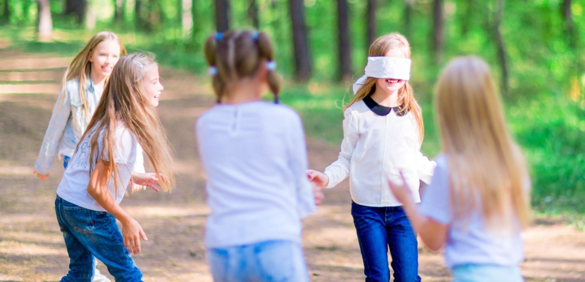 Fünf Mädchen spielen draußen, eins hat eine Augenbinde