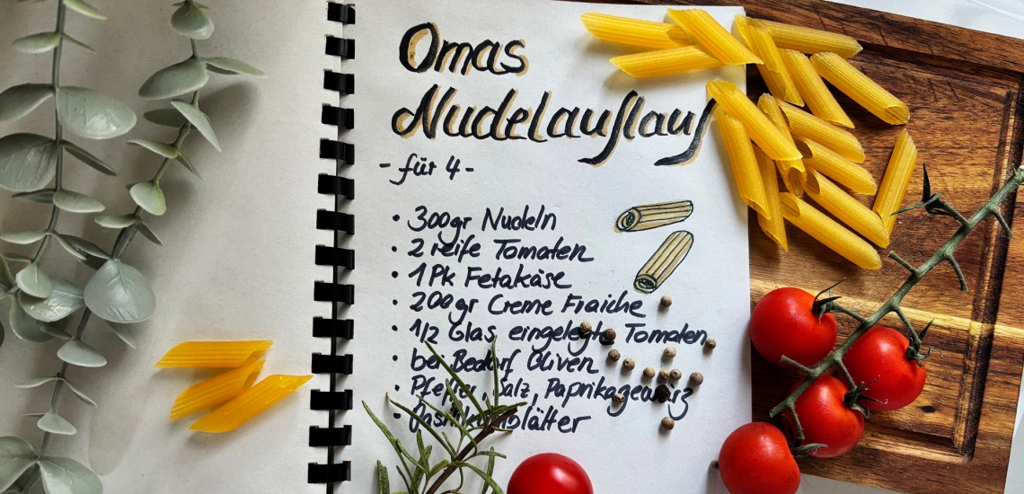 Innenseite eines Rezeptbuches mit Rezept für Omas Nudelauflauf, daneben Nudeln und Tomaten