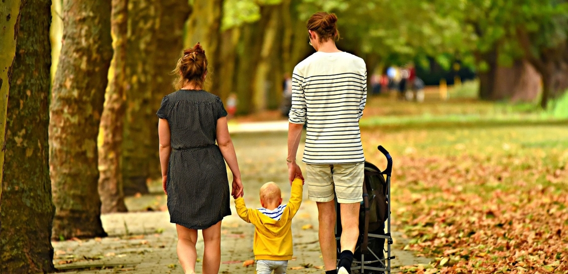 Mutter, Vater und Kleinkind gehen im Park spazieren