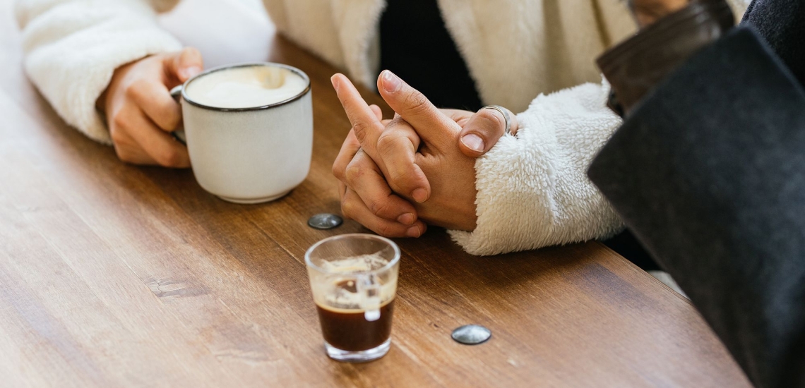Zwei Männer am Tisch halten sich an den Händen und trinken Kaffee