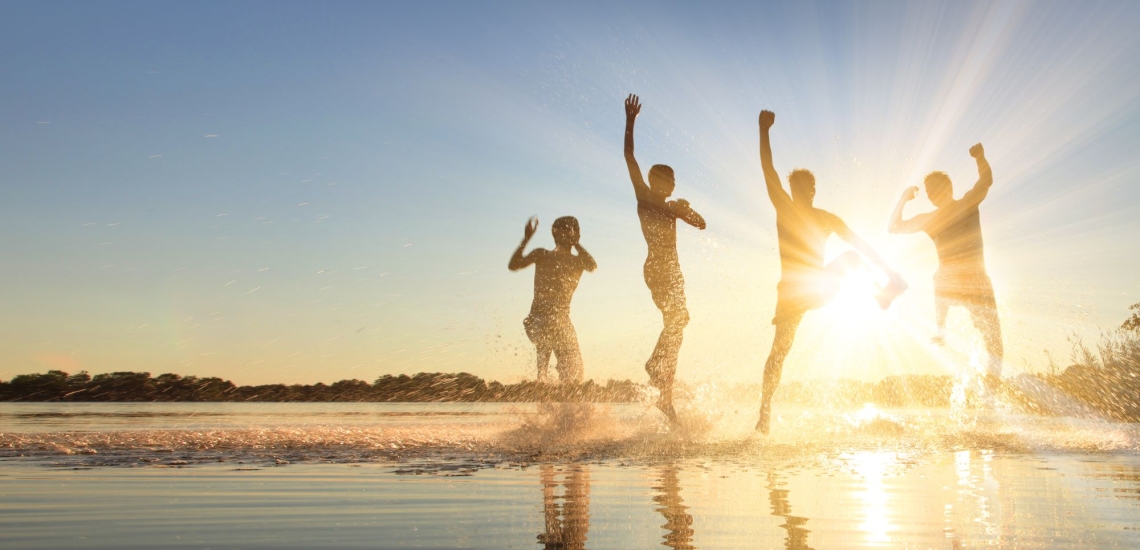 Jugendliche springen am See in der untergehenden Sonne im Wasser herum