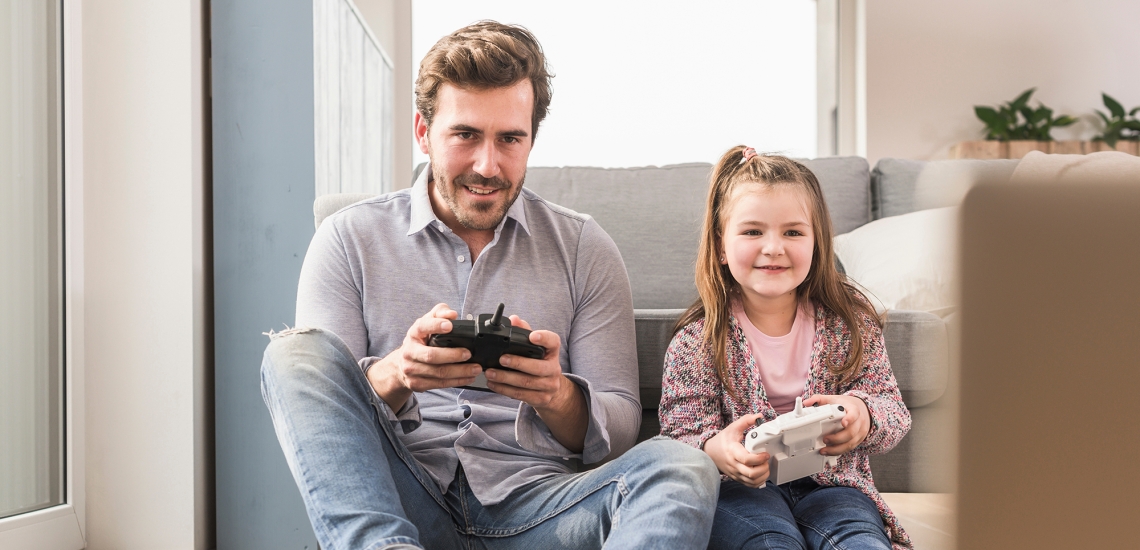 Ein Vater spielt mit seiner Tochter ein Computerspiel, beide halten eine Spielkonsole in der Hand.