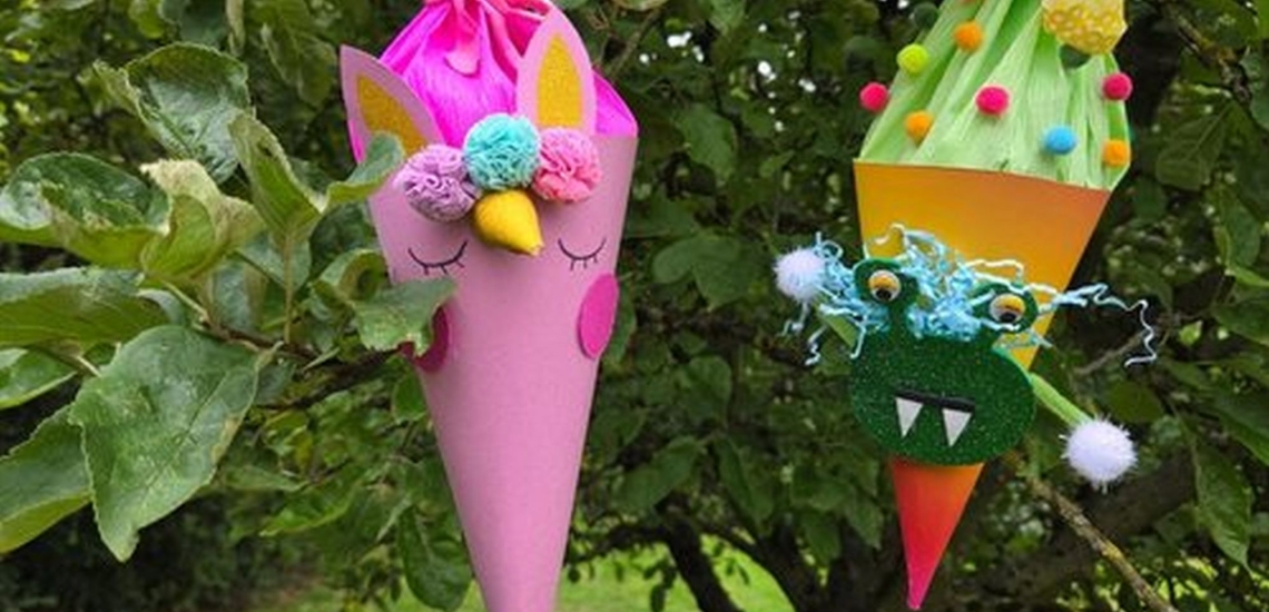 Kleine Schultüten in pink und und orange mit Augen, Zähnen und Pompons hängen in einem Baum