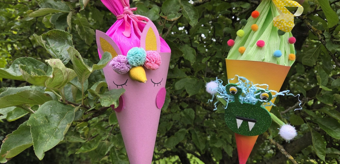 Kleine Schultüten in pink und und orange mit Augen, Zähnen und Pompons hängen in einem Baum