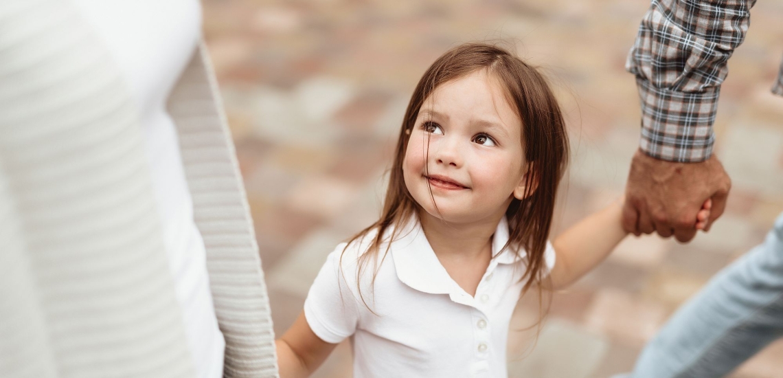 Kind geht zwischen Mutter und Vater und hält diese an der Hand