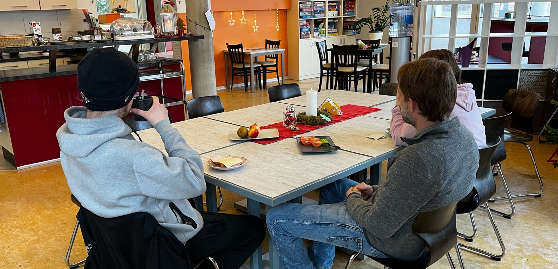 Drei Jugendliche von hinten fotografiert um einen Esstisch.