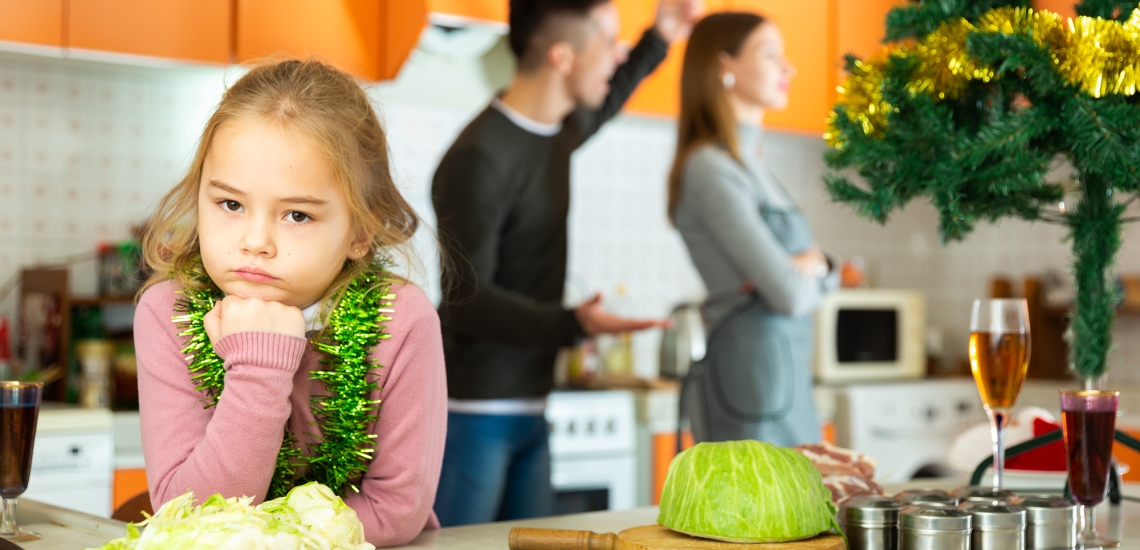 Ein Mädchen blickt in die Kamera, während im Hintergrund die Eltern streiten.