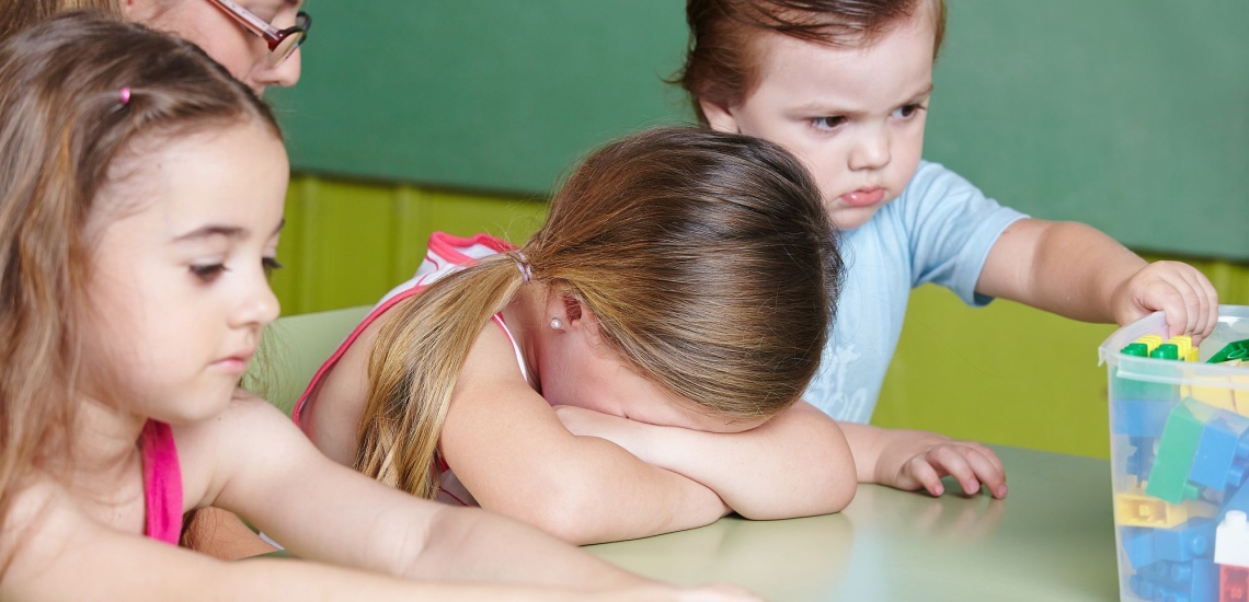 Kind weint in Kita, daneben andere Kinder und Erzieherin