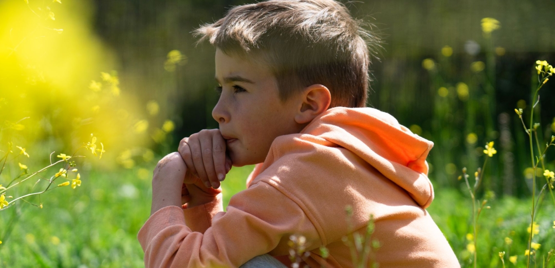 Junge sitzt nachdenklich im Gras in der Sonne