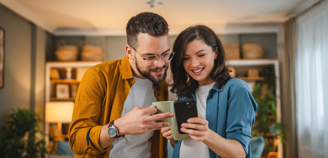 Ein Mann und eine Frau schauen gemeinsam auf ein Handy und lachen dabei.