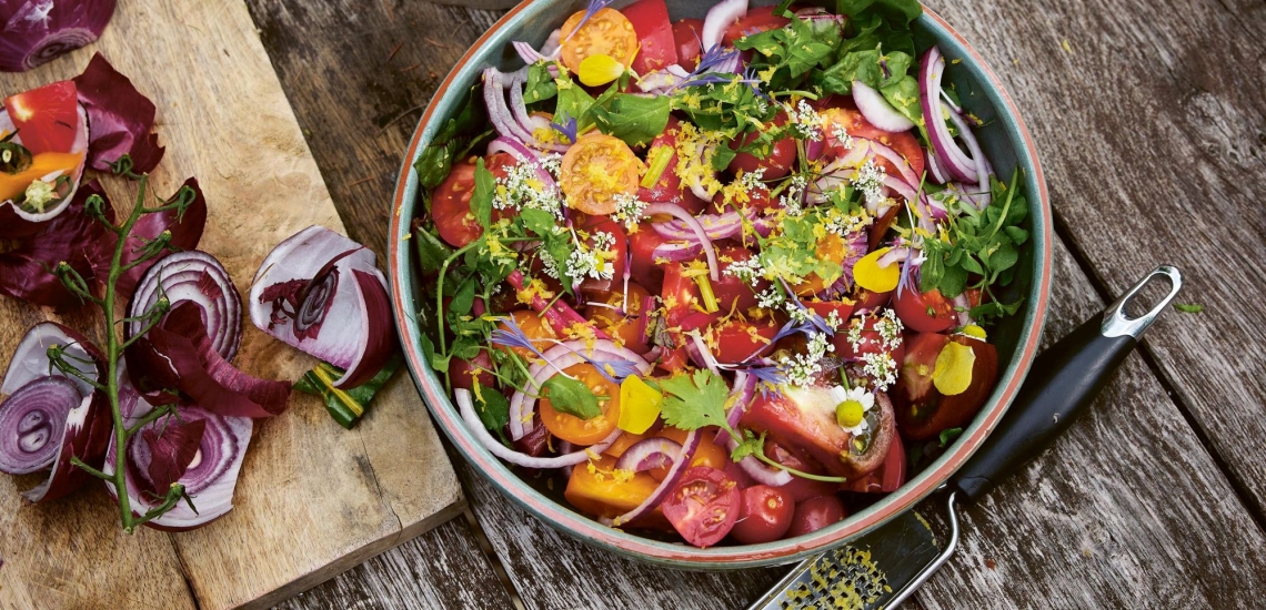 Tomatensalat mit Zwiebeln, Kräutern und Blüten in Schale auf Holztisch