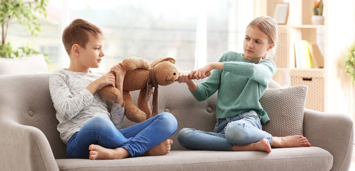 zwei Geschwister sitzen auf einem Sofa und ziehen an einem Stoffhasen