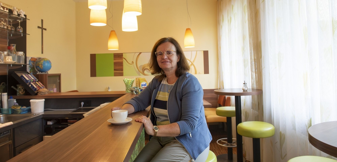 Frau sitzt in Cafe der Schule an Theke, vor sich einen Capuccino